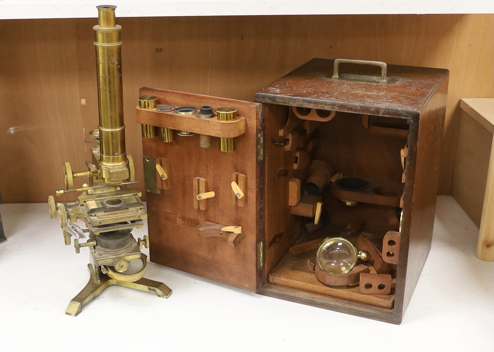A brass microscope with mahogany box by A. Ross of London, dated 1890 to foot, with some unusual features including a rotating box under the bed for lens, box with fitted interior containing additional lens and other att